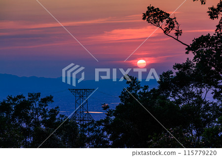 Evening view from the observation deck at 600m above sea level on the Shigiikoma Skyline, bordering Nara and Osaka prefectures. Medium telephoto zoom. The sun setting while dyeing the sky a deep red. 115779220
