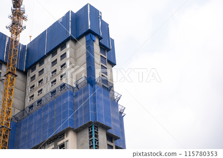 High-rise building under construction, wrapped in blue protection safety net High-rise building under construction, wrapped in blue protection safety net 115780353