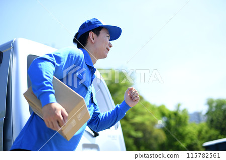A male delivery driver running outdoors carrying packages 115782561