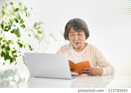 A senior woman using a computer while looking at her pension book 115785685