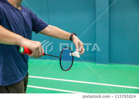 Badminton player hand serving holding shuttlecock and professional badminton racket at indoor sport badminton court 115785824