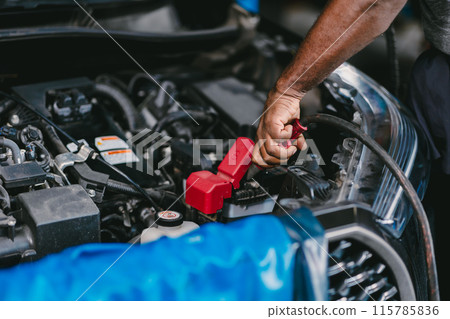 Closeup mechanic worker hand clamping car battery terminal for jump start low voltage battery vehicle in garage. 115785836
