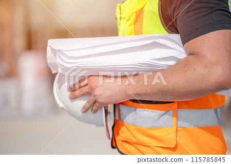 Closeup Engineer Construction Workers with Blueprint and Safety Hard hat at Building Site Closeup Engineer Construction Workers with Blueprint and Safety Hard hat at Building Site 115785845