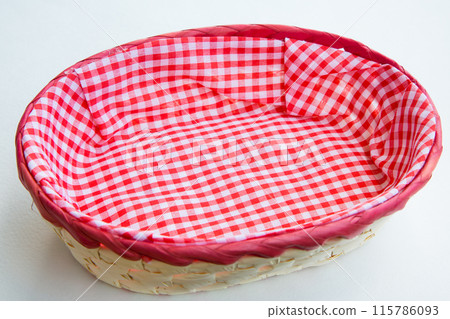 Wicker basket with red and white plaid cloth on white background 115786093