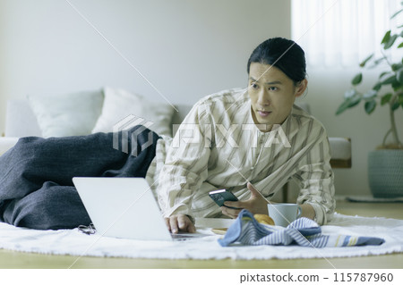 一名中年男子躺在客廳操作筆記型電腦和智慧型手機 115787960