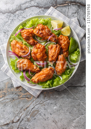 Thai Tom Yum Chicken served with onion, lime and lettuce closeup on the plate. Vertical top view 115789768