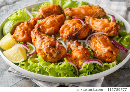Tom yum chicken wings deep fried served with onions and lime close up in a plate. Horizontal 115789777