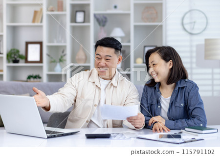 Young smiling Asian family, man and woman sitting at home at table in front of laptop and doing financial budget and documents. 115791102