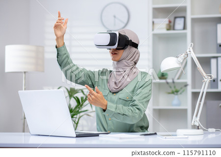 A young Muslim woman in a hijab sits in the office at a desk, wearing a virtual mask and talking remotely via online communication. A young Muslim woman in a hijab sits in the office at a desk, wearing a virtual mask and talking remotely via online communication. 115791110