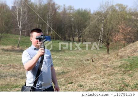 A young man videotaping on a smartphone. Uses gimbal to get smooth footage. Closely watching the movie shooting. A young man videotaping on a smartphone. Uses gimbal to get smooth footage. Closely watching the movie shooting. 115791159