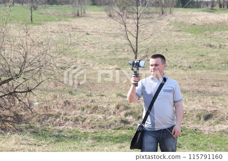 A young man videotaping on a smartphone. Uses gimbal to get smooth footage. Closely watching the movie shooting. 115791160