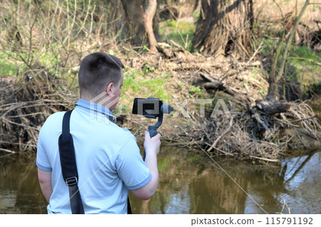 A young man videotaping on a smartphone. Uses gimbal to get smooth footage. Closely watching the movie shooting. 115791192