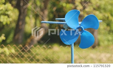 A blue vane weathervane spins in the wind in the summer. 115791320