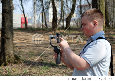 A young man videotaping on a smartphone. Uses gimbal to get smooth shots. Controls the recording by touching the screen. A young man videotaping on a smartphone. Uses gimbal to get smooth shots. Controls the recording by touching the screen. 115791478