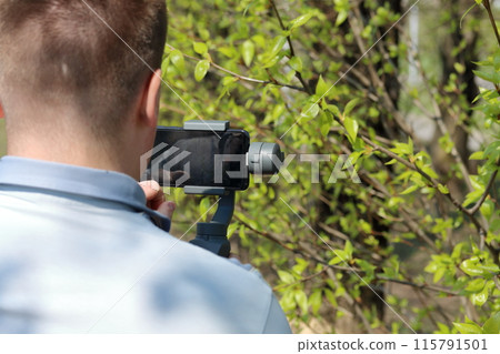 A young man videotaping on a smartphone. Uses gimbal to get smooth footage. Closely watching the movie shooting. A young man videotaping on a smartphone. Uses gimbal to get smooth footage. Closely watching the movie shooting. 115791501