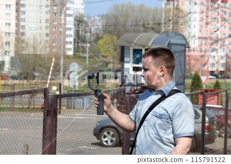 A young man videotaping on a smartphone. Uses gimbal to get smooth footage. Closely watching the movie shooting. A young man videotaping on a smartphone. Uses gimbal to get smooth footage. Closely watching the movie shooting. 115791522