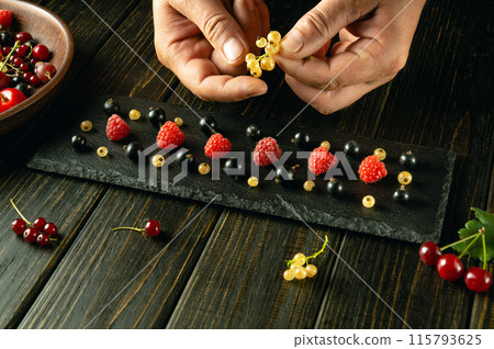 A cook arranging ripe different berries on a black sorting board before eating. Advertising space on blackboards A cook arranging ripe different berries on a black sorting board before eating. Advertising space on blackboards 115793625