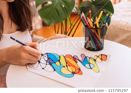 Lady paints over a drawing on a white sheet with colored pencils 115795297