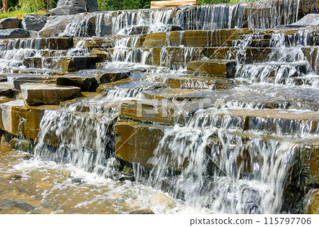 Close-up of stone steps of artificially created waterfall, water flowing on stone steps. 115797706