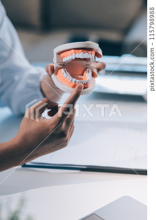 A dentist is using specialized dental equipment to inspect dentures to study the anatomy of the teeth before using the knowledge to treat patients, Dentures are being studied by oral specialists. 115798988