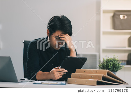 Frustrated Asian young businessman worker working on table in office. Busy employee worker people feel tired and headache from late work and overwork job document on computer desk at company workplace 115799178