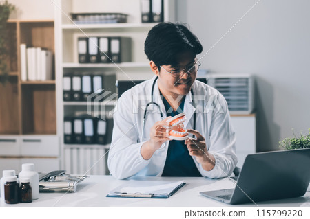 A dentist is using specialized dental equipment to inspect dentures to study the anatomy of the teeth before using the knowledge to treat patients, Dentures are being studied by oral specialists. 115799220