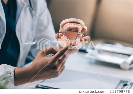 A dentist is using specialized dental equipment to inspect dentures to study the anatomy of the teeth before using the knowledge to treat patients, Dentures are being studied by oral specialists. A dentist is using specialized dental equipment to inspect dentures to study the anatomy of the teeth before using the knowledge to treat patients, Dentures are being studied by oral specialists. 115799778