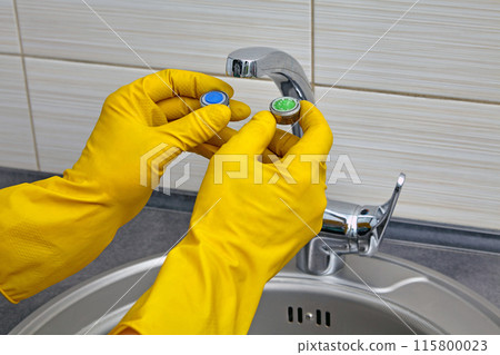 Plumber's hands in yellow rubber gloves change an old clogged kitchen sink faucet aerator to a new one Plumber's hands in yellow rubber gloves change an old clogged kitchen sink faucet aerator to a new one 115800023