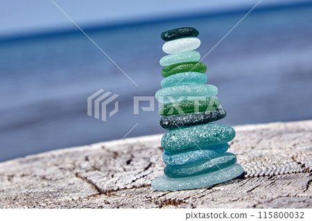 Stable balanced cairn of polished sea glass stones on a wooden log on the seashore Stable balanced cairn of polished sea glass stones on a wooden log on the seashore 115800032