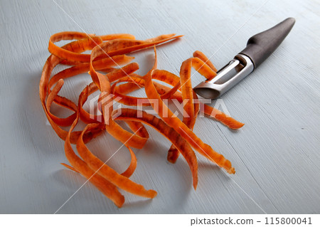 Carrot peelings and black metal peeler on a light wooden table Carrot peelings and black metal peeler on a light wooden table 115800041