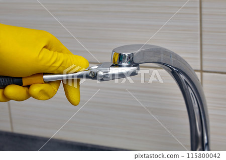 A plumber wearing yellow rubber gloves changes the faucet aerator. Regular repairs and replacement of water pipes 115800042
