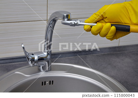 A plumber in yellow rubber gloves unscrews the faucet aerator with an adjustable wrench A plumber in yellow rubber gloves unscrews the faucet aerator with an adjustable wrench 115800043