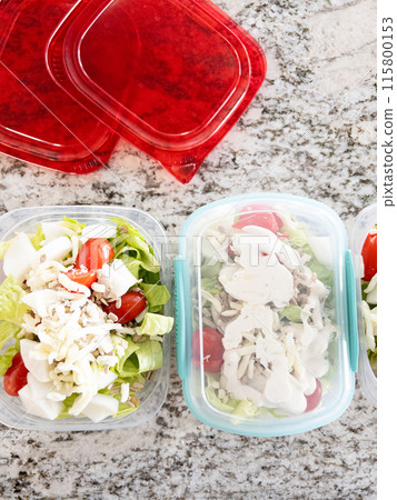 Containers filled with salad and dressing, prepared for convenient lunchtime meal prep. Containers filled with salad and dressing, prepared for convenient lunchtime meal prep. 115800153