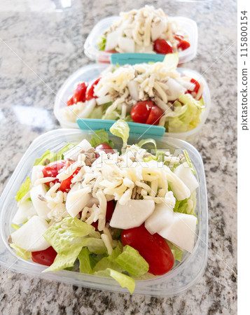 Containers filled with salad and dressing, prepared for convenient lunchtime meal prep. Containers filled with salad and dressing, prepared for convenient lunchtime meal prep. 115800154