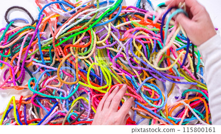 Flat lay. Hands meticulously organize a kaleidoscope of multicolored, patterned clay beads, intricately coiled and laid out against a stark white backdrop. Flat lay. Hands meticulously organize a kaleidoscope of multicolored, patterned clay beads, intricately coiled and laid out against a stark white backdrop. 115800161
