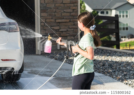 A young girl enthusiastically assists in washing the family's electric car in their suburban driveway. A young girl enthusiastically assists in washing the family's electric car in their suburban driveway. 115800162