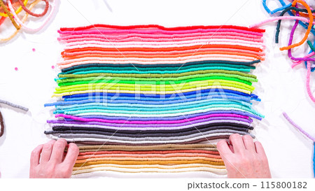 Flat lay. Hands touch a neatly organized rainbow of colorful, coiled clay bead strands against a contrasting white surface. Flat lay. Hands touch a neatly organized rainbow of colorful, coiled clay bead strands against a contrasting white surface. 115800182