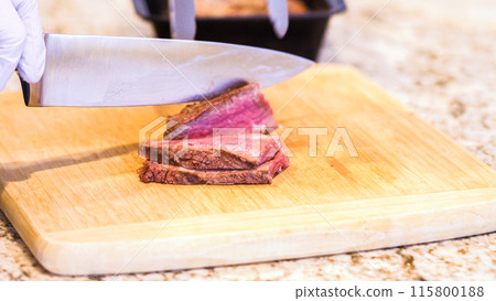 Gloved chef slices succulent pink steak on natural bamboo board, kitchen backdrop. Gloved chef slices succulent pink steak on natural bamboo board, kitchen backdrop. 115800188