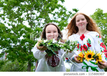 Two Ukrainian girls dance in embroidered shirts. Two women in authentic ukrainian clothes dancing outdoors in green summer fields. Two Ukrainian girls dance in embroidered shirts. Two women in authentic ukrainian clothes dancing outdoors in green summer fields. 115800307