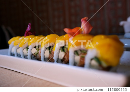 Sushi rolls are rotated in package after delivery. Philadelphia roll in sushi set close up. Traditional Japanese food. Japanese kitchen with sea food. Taking one sushi roll from set using chopsticks. Sushi rolls are rotated in package after delivery. Philadelphia roll in sushi set close up. Traditional Japanese food. Japanese kitchen with sea food. Taking one sushi roll from set using chopsticks. 115800333