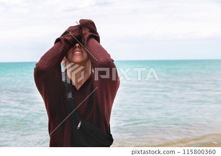 A young woman laughs hysterically covering her face with her hands on the sea beach in rainy weather. Ruined vacation A young woman laughs hysterically covering her face with her hands on the sea beach in rainy weather. Ruined vacation 115800360