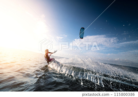 Attractive young Caucasian female kiteboarder doing a trick at sunset with splashes and a smile. Wide angle. Deep dive Attractive young Caucasian female kiteboarder doing a trick at sunset with splashes and a smile. Wide angle. Deep dive 115800386