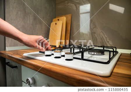 Women's hands turn on the gas stove. White gas stove in a home kitchen Women's hands turn on the gas stove. White gas stove in a home kitchen 115800435