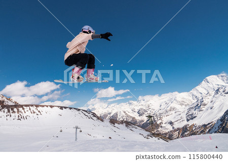young woman snowboarder jumping from a springboard in the snowy mountains 115800440