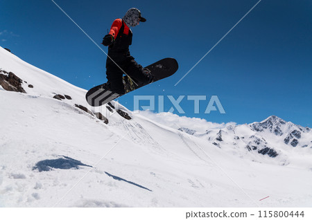A woman snowboarder makes a ski jump against the backdrop of high snow-capped mountains A woman snowboarder makes a ski jump against the backdrop of high snow-capped mountains 115800444