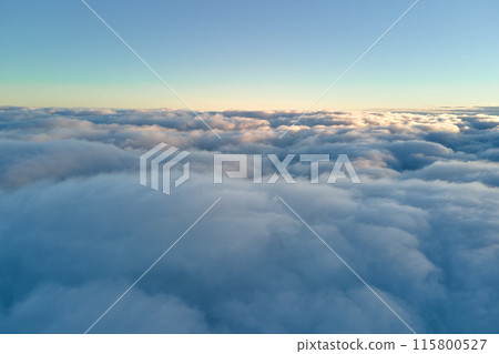 Aerial view from above at high altitude of dense puffy cumulus clouds flying in evening. Amazing sunset from airplane window point of view 115800527