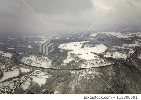 Aerial foggy landscape with mountain road covered with fresh fallen snow during heavy snowfall in winter mountain forest on cold quiet day Aerial foggy landscape with mountain road covered with fresh fallen snow during heavy snowfall in winter mountain forest on cold quiet day 115800591