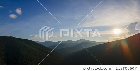Aerial view of dark mountain hills with bright sunrays of setting sun at sunset. Hazy peaks and misty valleys in evening 115800607