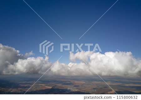 Aerial view from airplane window at high altitude of earth covered with white puffy cumulus clouds Aerial view from airplane window at high altitude of earth covered with white puffy cumulus clouds 115800632