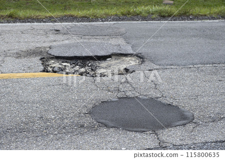 Damaged american road surface with deep pothole. Ruined street in urgent need of repair Damaged american road surface with deep pothole. Ruined street in urgent need of repair 115800635